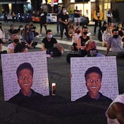 Deux personnes tiennent des affiches montrant des images représentant Elijah McClain pendant une veillée aux chandelles.