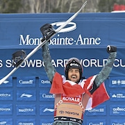 Éliot Grondin lève les bras au ciel en souriant sur le podium. 