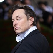 Elon Musk se retourne vers la caméra, en complet.