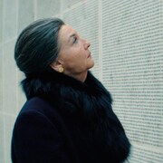 Une femme portant un manteau en fourrure regarde un mur commémoratif, dans une image du film Simone, le voyage du siècle.
