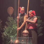 Émilie Monnet et Waira Nina, sur une scène, tiennent chacune un objet.