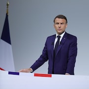 Le président Emmanuel Macron est debout derrière un pupitre et devant le drapeau européen et le drapeau français.
