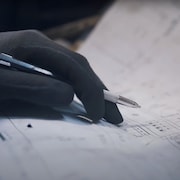 Une main tient un crayon sur un plan.