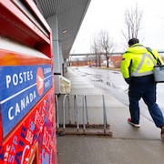 Un employé de Postes Canada marche à côté d'une boîte aux lettres.