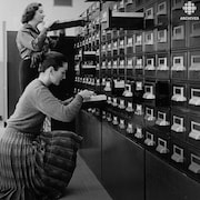 Deux employées, Jacqueline Farley et Charlotte Ferland, consultent des fiches dans un classeur.