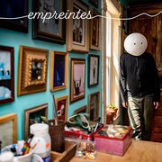 Ultra Nan avec un masque sur la tête dans son atelier. Au mur, on retrouve des dizaines de petits cadres avec ses oeuvres.