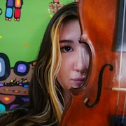 Image en 5 formats d'une jeune femme tenant un violon. En arrière-plan, une murale de l'artiste John Rombough sur le mur de l'école.
