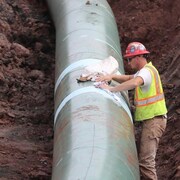 Un travailleur pose les dernières touches au pipeline, posé au fond d'un fossé de terre.