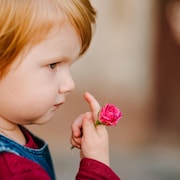 Petite fille rousse tenant une fleur dans sa main.