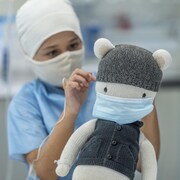 Un enfant de 9 ans assis dans un hôpital avec une perfusion, un masque et un bonnet.