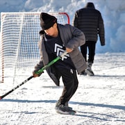 Un jeune garçon joue au hockey dans la rue enneigée.