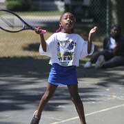 Une enfant fait un service dans un camps de tennis.