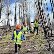 Des enfants marchent dans un sentier au milieu d'arbres brulés.