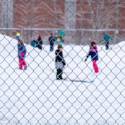 Des enfants de niveau primaire qui jouent sur une butte de neige dans un cour d'&eacute;cole.