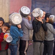 Des enfants palestiniens portent des casseroles alors qu'ils font la queue pour recevoir de la nourriture préparée par une cuisine caritative, dans un contexte de pénurie alimentaire.