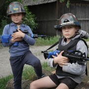 Deux jeunes garçons ukrainiens jouent aux soldats portant un casque et un fusil. 