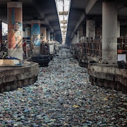 Un canal bouché par des contenants de polystyrène et de plastique à usage unique sous un pont.