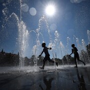 Des enfants se rafraîchissent en courant à travers une fontaine publique à Colmar, dans l'est de la France, le 21 août 2023. 