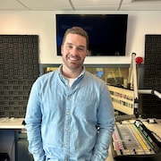 Un homme en chemise qui sourit à la caméra se tient debout dans un studio de radio.