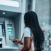 Une femme s'apprête à insérer sa carte dans un guichet automatique bancaire.