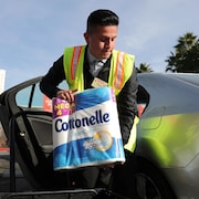 Un employé portant une veste jaune s'approche d'une voiture avec un méga paquet de papier de toilette Cottonelle.