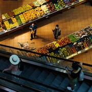 Des gens magasinent dans le rayon des fruits d'une épicerie.