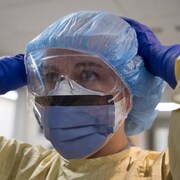 Une femme couverte avec des équipements de protection (masque, lunettes, couvre cheveux, gants et blouse).