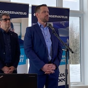 Deux hommes debout sur une scène avec des bannières du Parti conservateur du Québec derrière eux