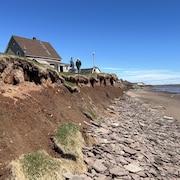 Renald Guinard et Bernard Savoie sont debout près de la falaise. Derrière eux, il y a la maison de M. Guignard. Devant, la plage et la mer.