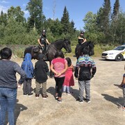 Une dizaine d'enfants de dos admirent deux policières à cheval.