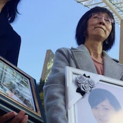 Une femme tient un cadre avec une photo, devant le Palais de Justice.