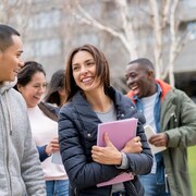 Cinq étudiants internationaux discutent en marchant sur un campus universitaire. 