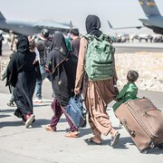 Des femmes et des enfants marchent sur le tarmac d’un aéroport.