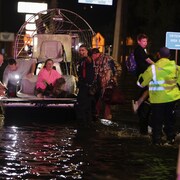 Plusieurs personnes poussent une femme assise dans un hydroglisseur avec des animaux dans une rue inond&eacute;e.