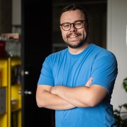 Un homme prend la pose, souriant, les bras croisés. 