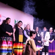 Des femmes sont alignées lors d'une cérémonie. Une femme purifie une plume. 