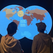 Deux garcons observent une carte du monde animée. 