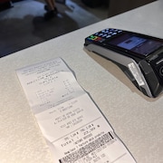 Une facture de restaurant sur une table à côté d'un terminal de paiement électronique.