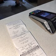 Une facture de restaurant sur une table à côté d'un terminal de paiement.