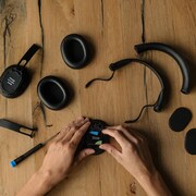 Deux mains posées sur un casque d'écoute démantibulé sur une table en bois. 