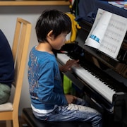 Un homme est assis devant son ordinateur, tandis qu'un enfant dos à lui joue du piano.