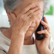 Une femme âgée parle au téléphone, elle semble soucieuse.