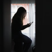 Une femme consulte son t&eacute;l&eacute;phone cellulaire avec attention.