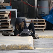 Une femme itinérante assise par terre au bord d'une rue.