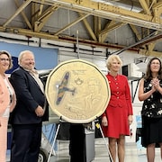 Quatre personnes à côté d'une grosse maquette de monnaie de 1 dollar.