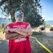 Un homme qui a les bras croisés montre ses tatouages sur ses avant-bras. Son visage est en partie peint en bleu.