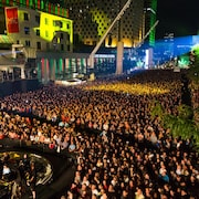 Une foule rassemblée sur la place des Festivals à Montréal la nuit. 