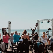 Un musicien salue le public qui l'acclame. Le concert a lieu en plein air, face à la mer.