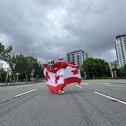 Un homme, de dos, avec un gros drapeau de la fête du Canada.