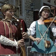 Deux femmes vêtues de costumes de l'époque de la Nouvelle-France jouent du biniou et du violon.